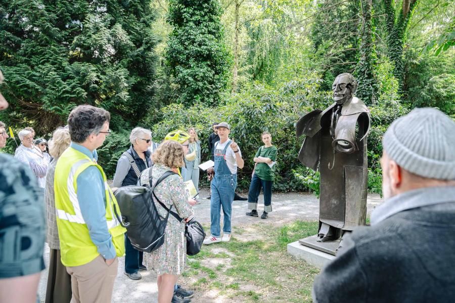 Gids geeft uitleg aan pubiek bij een sculptuur.