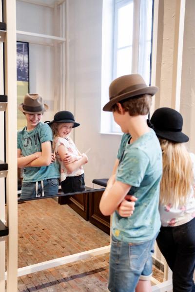 Twee kinderen met een oude hoed poseren lachend voor de spiegel