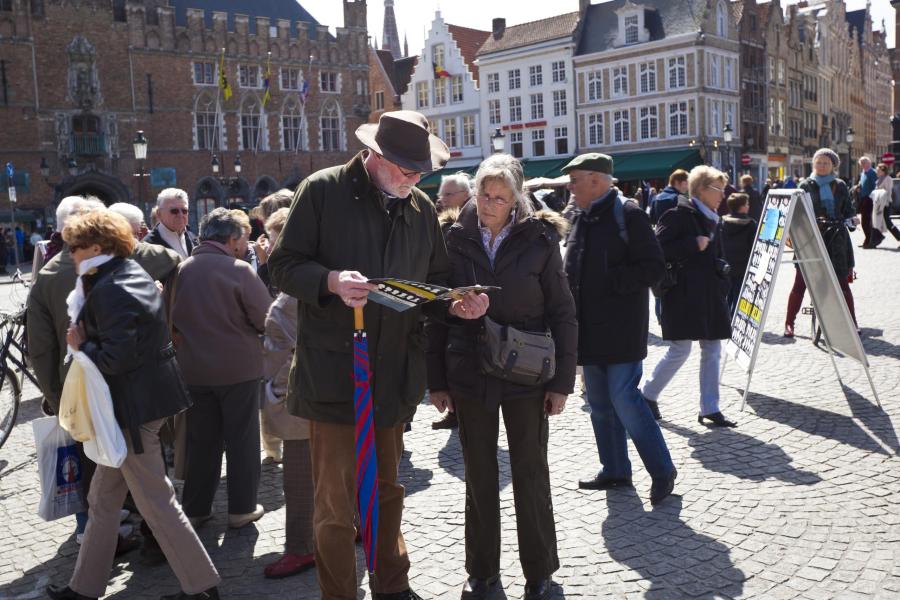 Een man en vrouw staan op de Markt in Brugge en lezen een foldertje.