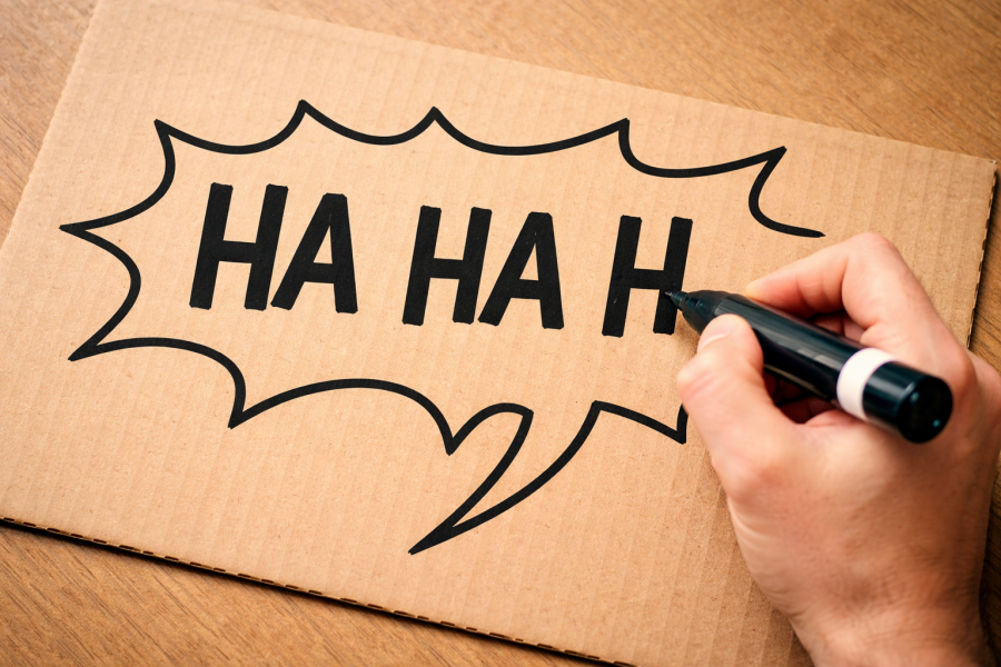 Je ziet een hand die op karton HA HA schrijft met een dikke stift